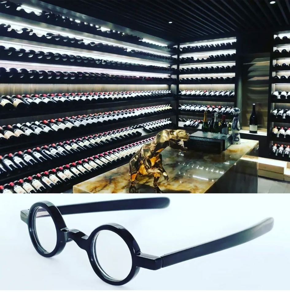 Black Harvey Taylor frames displayed beneath a wall of wine bottles
